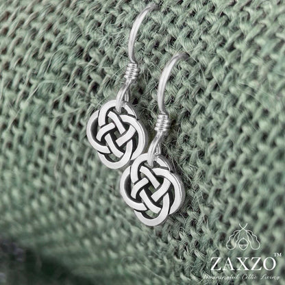 Tiny silver Dara knot earrings on sterling silver French wire. Shown on green background